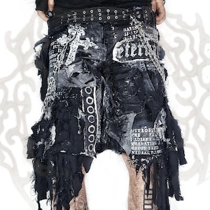 Peut inclure: Short en jean noir vieilli avec des bords effilochés, des finitions brutes et une chaîne en métal argenté. Le short est orné d'inscriptions blanches, d'une grande croix imprimée et d'une ceinture noire à œillets et boucles métalliques.