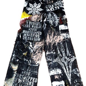 May include: Black and white printed pants with distressed details. The pants feature various graphic designs, including text and abstract shapes, with accents of yellow and pink. The text includes the words "BURNE", "WORLD", "WORSHIPPED", and "SORROW".