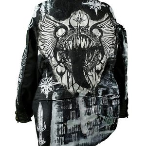 Puede incluir: Chaqueta negra y blanca con un estampado gráfico de una criatura alada con una boca grande y dientes. La chaqueta tiene un aspecto desgastado y presenta una variedad de textos y símbolos.