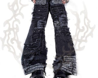 May include: Black distressed denim trousers featuring a wide-leg silhouette, heavy fraying, and layered fabric panels. The garment is adorned with white printed text patterns throughout, including the waistband and cuffs, paired with black platform shoes.