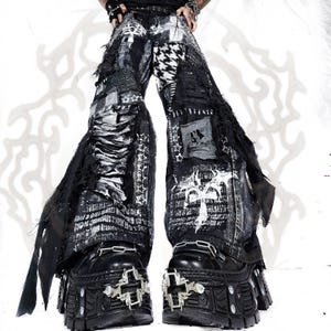 Könnte beinhalten: Schwarz-weiße, distressed Hose mit weitem Bein, Patchwork-Design, Sternenmustern, Text und ausgefransten Kanten. Die Hose wird mit schwarzen Plateaustiefeln kombiniert, die auf der Vorderseite silberfarbene kreuzförmige Beschläge haben.