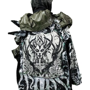 Könnte beinhalten: Eine schwarz-weiße Kapuzenjacke mit einem grafischen Druck eines Wesens mit Hörnern und Rosen. Die Jacke hat ein grünes Futter und eine schwarze Kapuze.