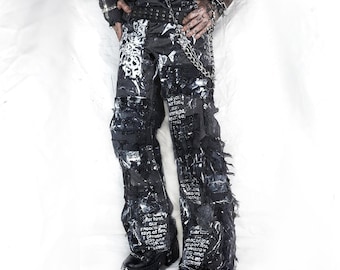 May include: Black and white patterned trousers with distressed detailing. The trousers feature a chain and belt, and are worn with black platform boots. The design includes printed text and a unique, edgy aesthetic.