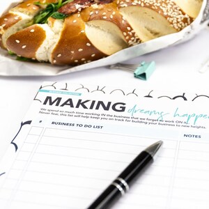 May include: A white sheet of paper with the text "MAKING dreams happen" printed in black. The paper has a business to do list with a section for notes and a priority rank. A black pen is lying on the paper.