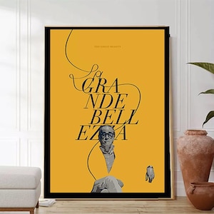 Puede incluir: Un póster amarillo con texto negro que dice "La Grande Bellezza" y una foto en blanco y negro de un hombre. El póster está enmarcado en un marco negro.