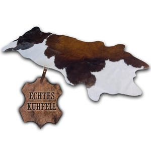 Könnte beinhalten: Kuhfellteppich mit einem natürlichen Muster aus Braun, Schwarz und Weiß. Der Teppich hat eine unregelmäßige Form und ein Etikett mit der Aufschrift "ECHTES KUHFELL". Dieser Teppich eignet sich für die Inneneinrichtung.