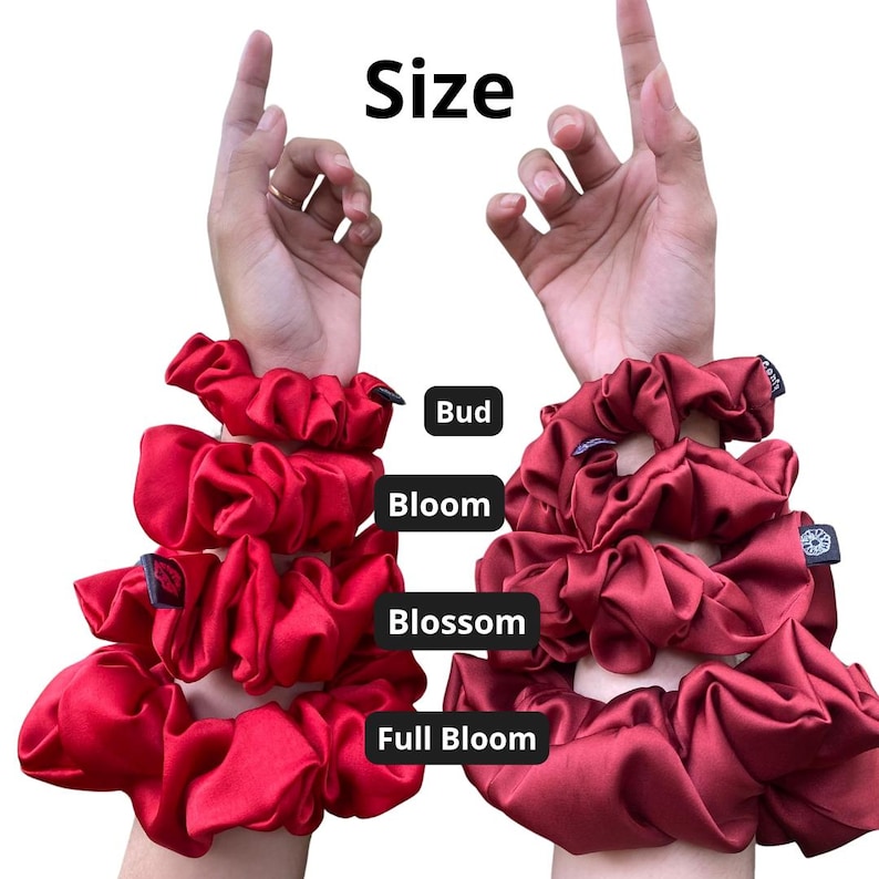 May include: A collection of red and dark red satin hair scrunchies arranged in four sizes labelled Bud, Bloom, Blossom, and Full Bloom. The scrunchies are displayed in a vertical stack on two arms, showing varying degrees of fabric fullness and volume.
