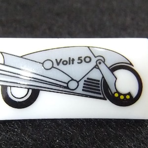 Könnte beinhalten: Eine weiße Keramikfliese mit einer Schwarzweißillustration eines futuristischen Motorrads. Das Motorrad hat einen silbernen Körper und schwarze Räder. Der Text "Volt 50" ist auf der Seite des Motorrads aufgedruckt.