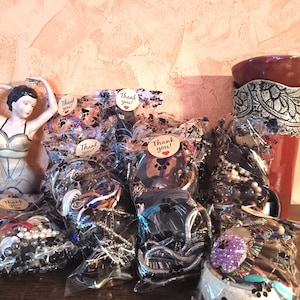 Könnte beinhalten: Eine Sammlung verpackter Armbänder und Accessoires, einige mit "Thank you!" Aufklebern. Die Armbänder befinden sich in transparenten Plastiktüten und zeigen verschiedene Farben und Designs. Eine dekorative Figur und eine rote Vase sind ebenfalls sichtbar.