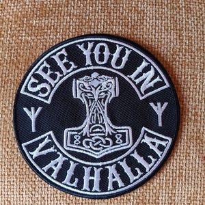 May include: A black and white embroidered patch with the text "See You In Valhalla" in a circular design. The patch features a stylized hammer with a knot design.