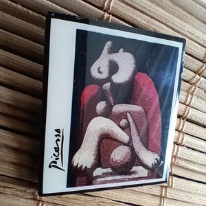 Könnte beinhalten: Rechteckiger Magnet mit einem Picasso-Kunstwerk. Das abstrakte Bild zeigt weiße, rote und braune Formen vor schwarzem Hintergrund. Die Signatur des Künstlers, "Picasso", ist in schwarzer Schrift in der unteren linken Ecke.