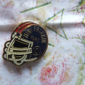 Könnte beinhalten: Eine blaue und weiße Emaille-Anstecknadel mit goldener Umrandung. Die Anstecknadel zeigt einen Footballhelm und den Text "Mini Frique Paris".
