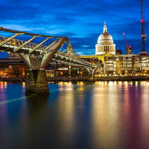 Puede incluir: Una vista nocturna del Puente del Milenio en Londres, con la Catedral de San Pablo al fondo. El puente está iluminado y el agua de abajo refleja las luces.