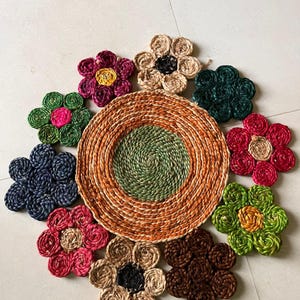 May include: A set of colourful woven flower-shaped mats, with a larger circular mat in the centre. The mats are made of natural fibres and have a rustic, handmade look.