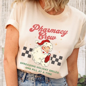 May include: A cream colored t-shirt with the text "Pharmacy Crew" in red and green lettering. A cartoon image of Santa Claus holding a bottle of pills is below the text. The text "Spreading Holiday Smiles One Pill At A Time" is below the image.