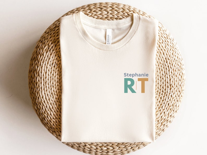 May include: A cream colored t-shirt with the text "Stephanie RT" in blue, green, and orange.