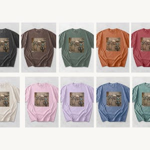 May include: A collection of ten short-sleeved t-shirts in various colors, including black, brown, green, orange, and pink. Each shirt features a graphic print of raccoons on motorcycles. The shirts are displayed on a white background.