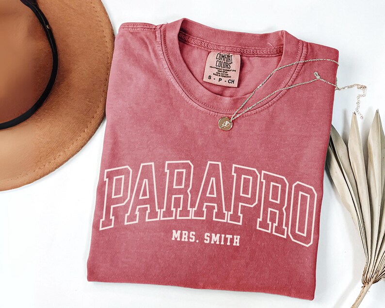 May include: A red t-shirt with the text "PARAPRO MRS. SMITH" in white. The shirt has a distressed look and is made of a soft, comfortable fabric.