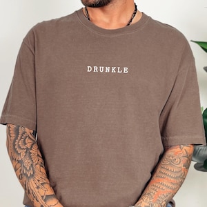 May include: A brown t-shirt with the word "DRUNKLE" printed in white on the front.