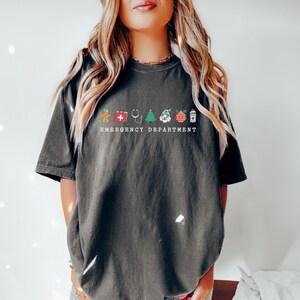 Peut inclure: Un t-shirt gris fonc&eacute; avec un motif blanc d'ic&ocirc;nes de No&euml;l et le texte "Emergency Department".