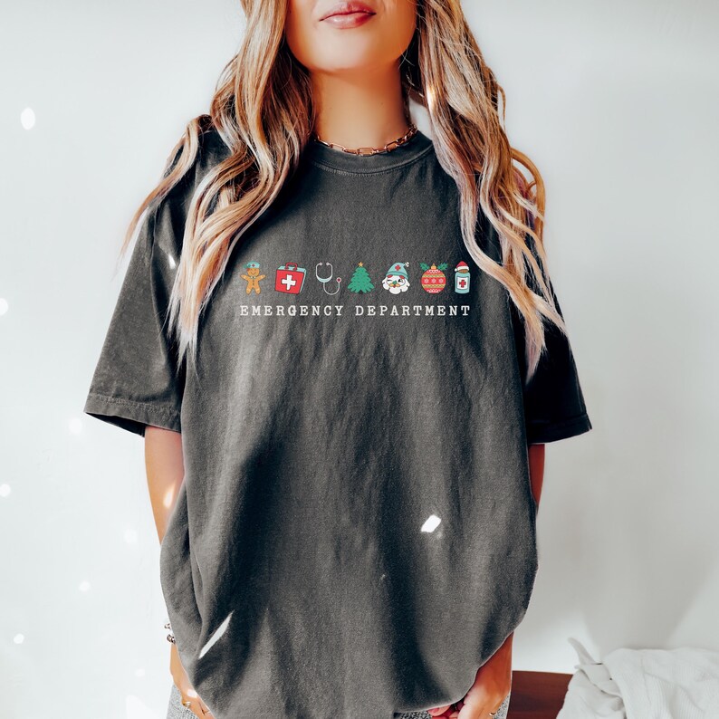 Peut inclure: Un t-shirt gris fonc&eacute; avec un motif blanc d'ic&ocirc;nes de No&euml;l et le texte "Emergency Department".