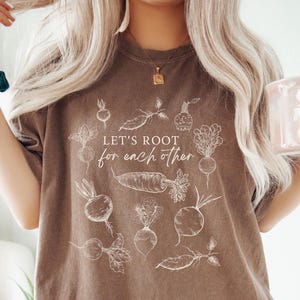 May include: A brown t-shirt with a white graphic of vegetables and the text "Let's root for each other".