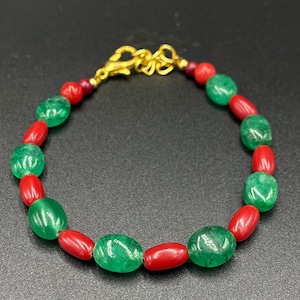Puede incluir: Un brazalete de cuentas verdes y rojas con un cierre dorado. El brazalete está hecho de cuentas ovaladas.