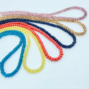 May include: A set of colourful glass bead necklaces in shades of blue, yellow, orange, and brown. The necklaces are made of small, round beads and are arranged in a rainbow pattern.