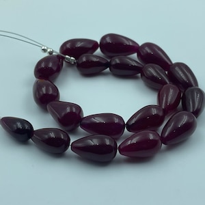 May include: A strand of deep red gemstone beads in a teardrop shape. The beads are strung on a silver wire.