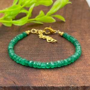 Puede incluir: Un brazalete de piedras preciosas verdes con un cierre dorado. El brazalete está hecho de pequeñas cuentas facetadas.