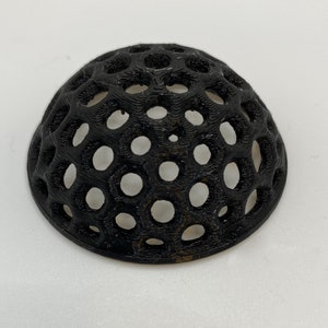 May include: A black plastic dome-shaped object with a honeycomb pattern. The object has many small holes throughout the surface.