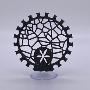 May include: A black 3D printed decorative object with a geometric design and a flower in the center. The object is on a clear suction cup base.