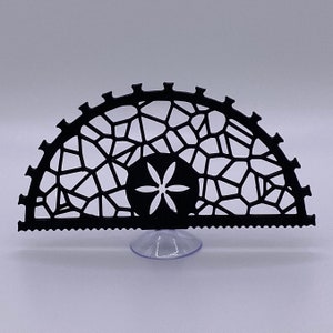 May include: Black metal decorative stand with a geometric design and a suction cup base. The stand is shaped like a half circle and features a floral pattern.