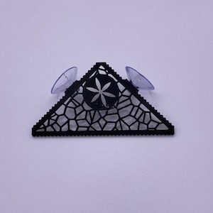 May include: Black triangular shelf with a geometric design and a flower in the center. The shelf has two suction cups on the back.