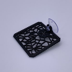 May include: Black geometric patterned suction cup, a decorative accent for a window or mirror.