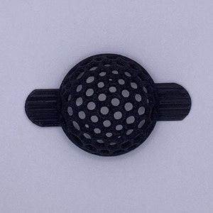 May include: A black plastic filter with a round, honeycomb-like design. The filter has two flat, rectangular tabs on either side.