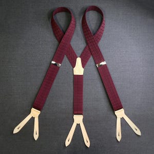 Può includere: Bretelle bordeaux con un motivo strutturato. Le bretelle hanno regolatori in metallo argentato e linguette in pelle color crema per il fissaggio ai pantaloni. Il design presenta uno stile a Y.