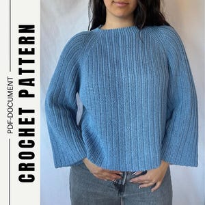 Op de afbeelding: Een lichtblauwe trui met lange mouwen, een verticaal geribbelde textuur, een ronde halslijn en raglanmouwen. De afbeelding bevat de tekst CROCHET PATTERN en PDF-DOCUMENT die verticaal aan de linkerkant van het kader wordt weergegeven.