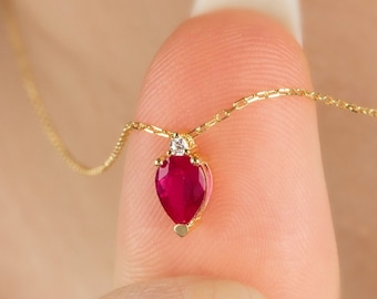 May include: A gold chain necklace with a heart-shaped pendant featuring a red ruby and a small diamond accent.