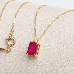 May include: A gold chain necklace with a red gemstone pendant. The pendant is set in a gold frame and has a small diamond accent.