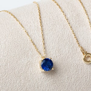 May include: A gold chain necklace with a blue gemstone pendant. The chain is delicate and the pendant is round.