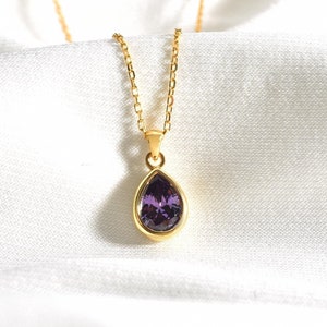 Könnte beinhalten: Eine goldene Kettenkette mit einem tropfenförmigen Anhänger mit einem violetten Edelstein.