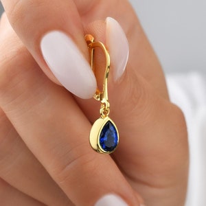 Op de afbeelding: Gouden druppel oorbel met een blauwe edelsteen.