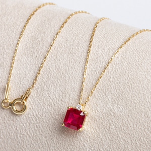 May include: A gold chain necklace with a square red gemstone pendant accented with smaller clear gemstones.