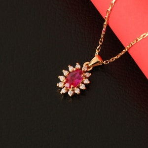 May include: A gold necklace with a red gemstone pendant surrounded by smaller clear gemstones. The necklace is on a black and red background.