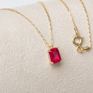 May include: A gold chain necklace with a red gemstone pendant. The pendant is a rectangular cut gemstone with a gold setting.