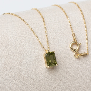 May include: A gold chain necklace with a green gemstone pendant. The pendant is a rectangular emerald cut.