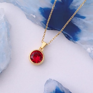May include: A gold chain necklace with a red gemstone pendant. The pendant is round and has a smooth, polished finish.