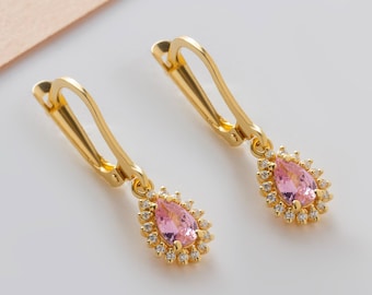 May include: A pair of gold earrings with pink pear-shaped stones surrounded by smaller clear stones.