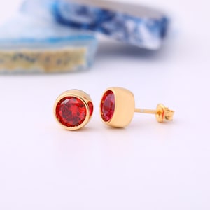 May include: A pair of gold stud earrings with red round gemstones.
